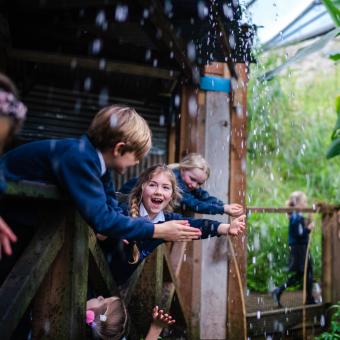 A group of school pupils leaning over the wooden railings to touch the rain water falling